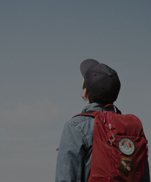 Student with red backpack and a cap looking up